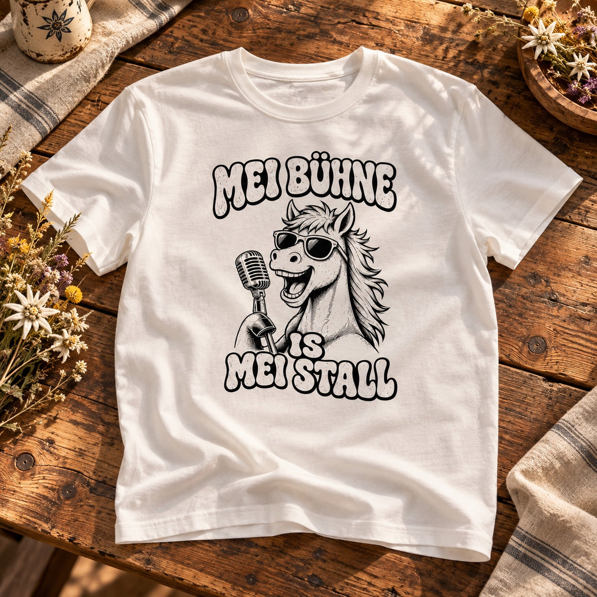 Weißes Pferdebua-Herrenshirt mit Pferd, Sonnenbrille, Mikrofon und „Mei Bühne is mei Stall“ auf einem Holztisch