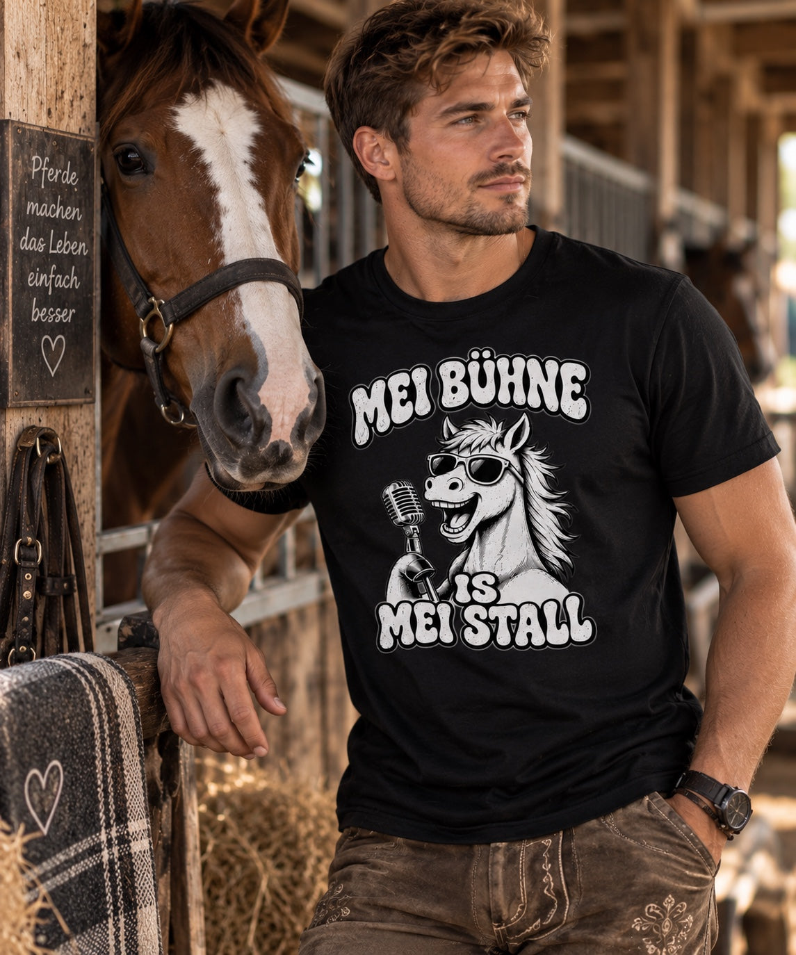 Mann trägt schwarzes Pferdebua-Shirt mit Pferdemotiv neben einem Pferd im Stall