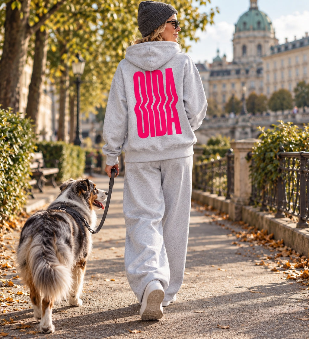 Frau trägt grau melierten OIDA Hoodie mit pinkem Rückenprint beim Hundespaziergang