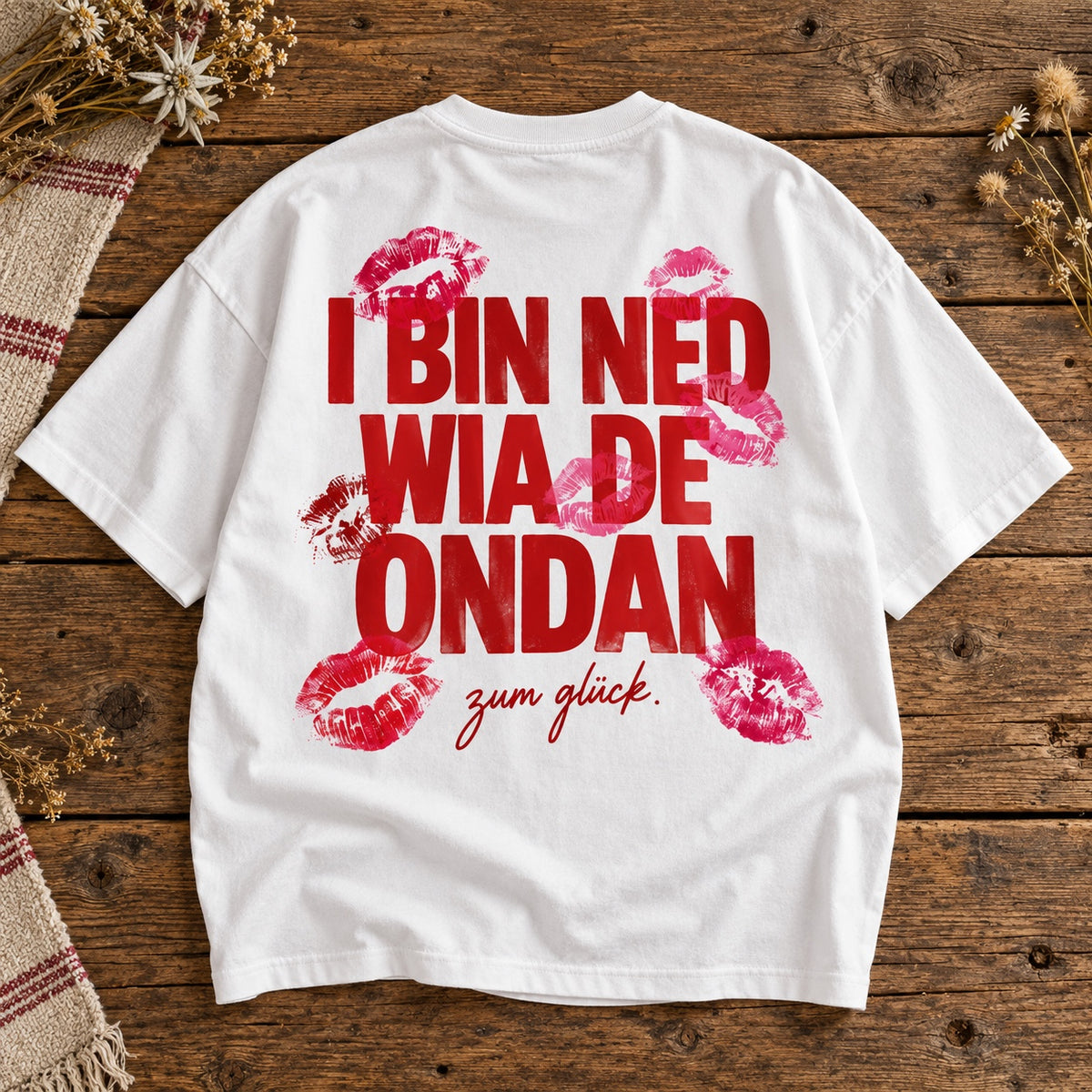 Weißes Damen Oversize-T-Shirt mit rotem Schriftzug I bin ned wia de ondan – zum Glück und Kussmundmotiven auf Holztisch