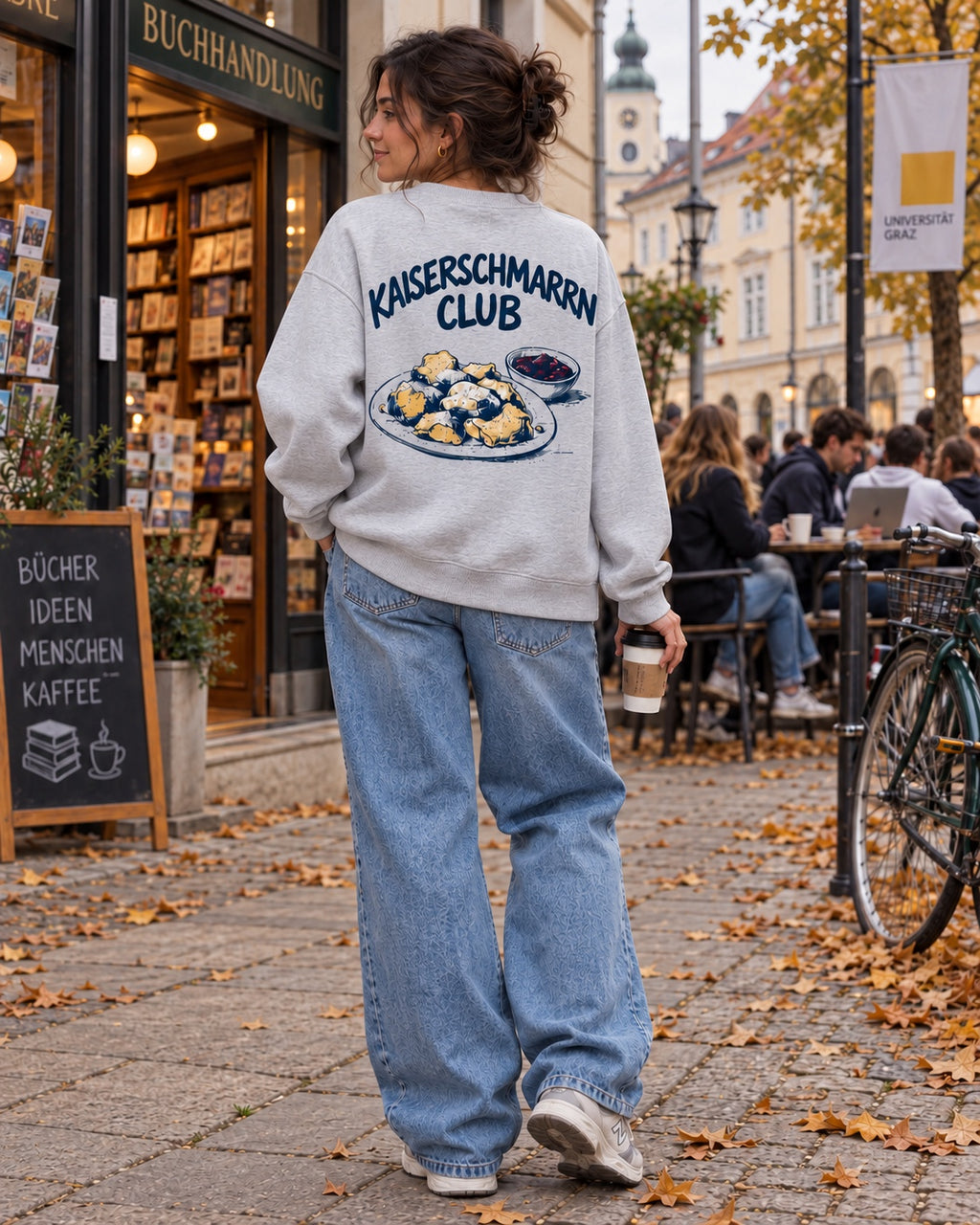 Damen Oversize-Rundhalspullover Kaiserschmarrn Club in Grau meliert – Model vor einer Buchhandlung