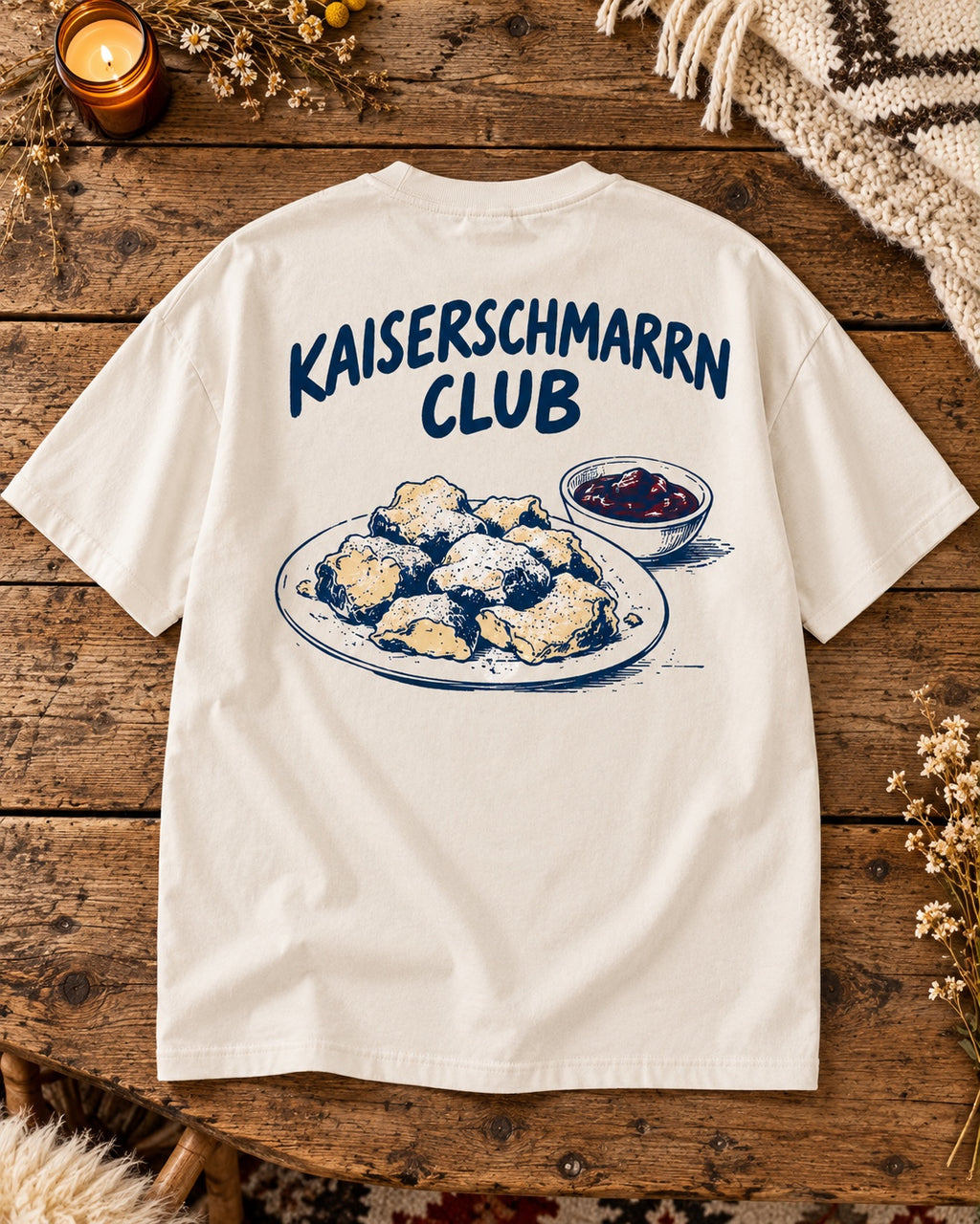 Weißes Oversize-T-Shirt Kaiserschmarrn Club auf einem Altholztisch – Rückenmotiv