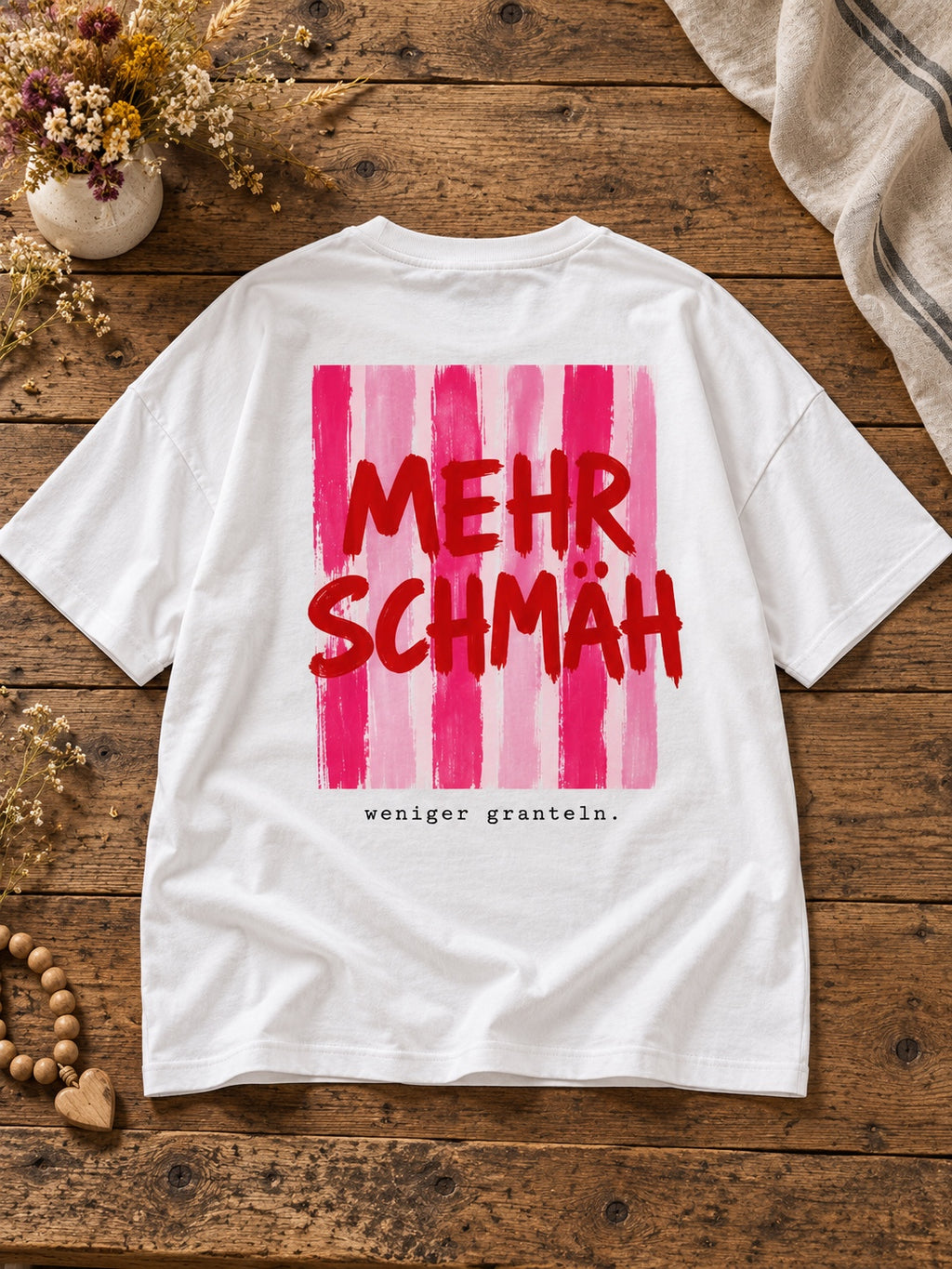 Weißes Damen Oversize-T-Shirt Mehr Schmäh – weniger granteln mit pink-rotem Rückenprint auf Altholztisch