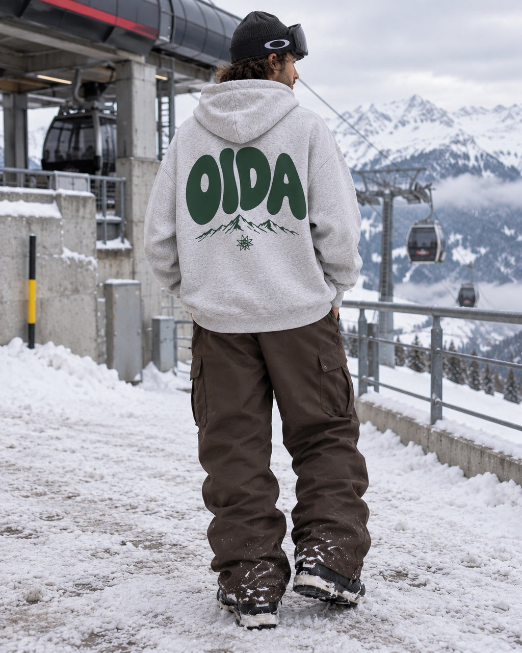 Männliches Model mit grauem OIDA Oversize-Hoodie an einer Bergstation