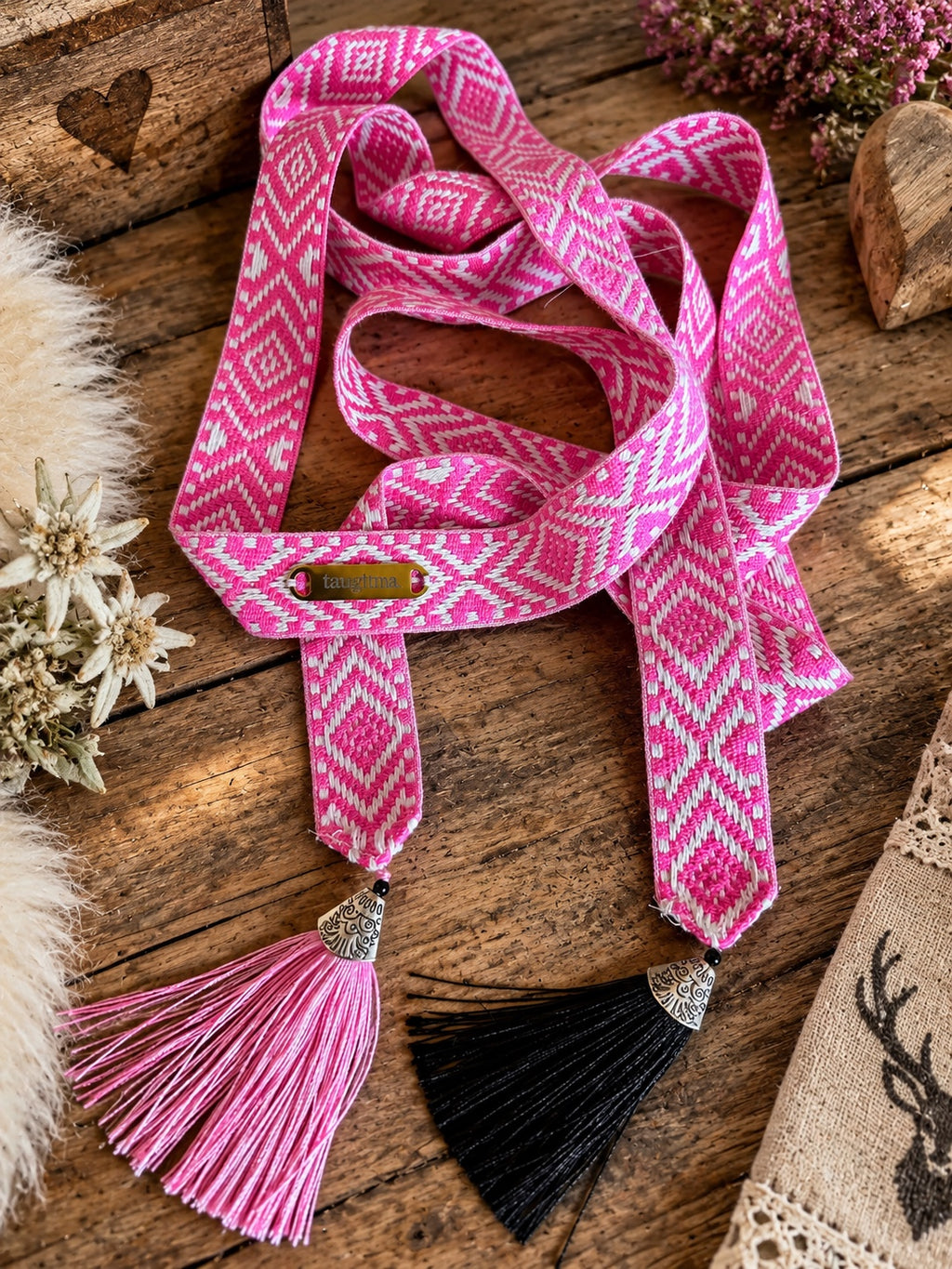 SCHMIGI Taillengürtel in Pink und Weiß mit pinker und schwarzer Quaste auf einem Altholztisch
