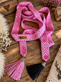 SCHMIGI Taillengürtel in Pink und Weiß mit pinker und schwarzer Quaste auf einem Altholztisch